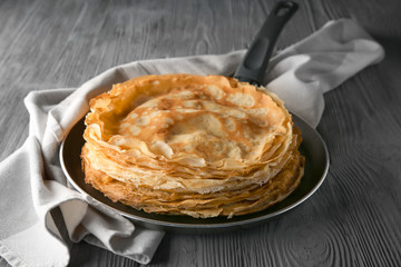 Frying pan with stack of delicious thin pancakes on wooden table