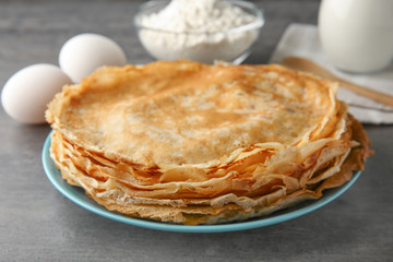 Plate with stack of delicious thin pancakes on table