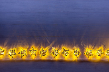 Christmas lights yellow stars burn on dark ultramarine wooden background. New Year festive home...