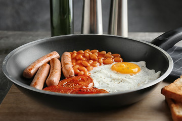 Frying pan with egg, beans, sausages and tomatoes on table