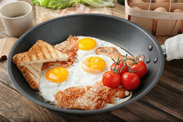 Frying pan with eggs, bacon, toasts and cherry tomatoes on table