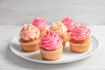 Plate with yummy cupcakes on wooden table
