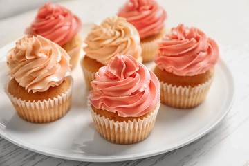 Plate with yummy cupcakes on wooden table