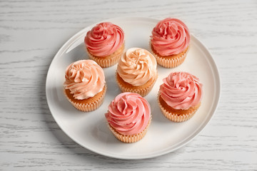 Plate with yummy cupcakes on wooden table
