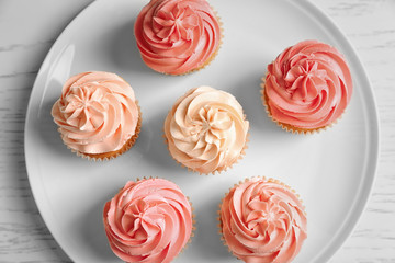 Plate with yummy cupcakes on wooden table