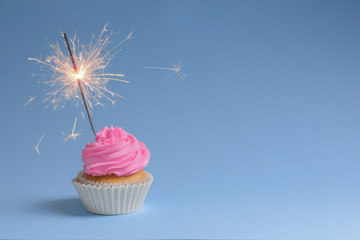 Yummy cupcake with sparkler on color background