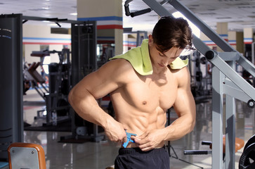 Naklejka na ściany i meble Muscular young man using body fat caliper in gym
