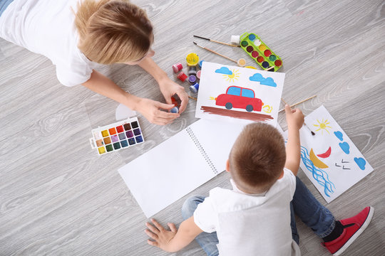 Mother with cute boy painting picture on sheet of paper, indoors