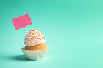 Delicious cupcake with greeting card on color background