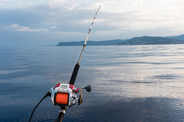 electric fishing reel mounted on a rod with sea in the background and orange line