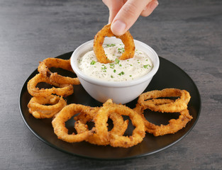 Woman dipping onion ring into bowl with sauce on table