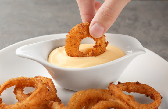Woman dipping onion ring into gravy boat with sauce on table
