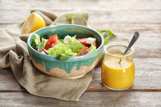 Bowl with salad and jar of tasty sauce on table