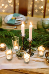 decor, illumination, wedding concept. wooden table of fair color served and decorated with lots of burning candles of differen kinds and forms, they are placed by fresh branches of green fluffy