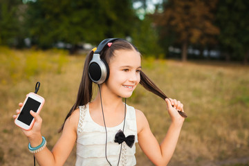 active girl with long hair having nice rest outdoor, little girl with black and silver headphone listening song on nature