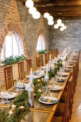 winter, meeting, holidays concept. extremely long wooden table in the restaurant hall for calebrating with lovely windows, there are lots of candles and aromatic conifer branches