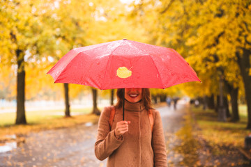 Happy woman with red umbrella walking at the rain in beautiful autumn park