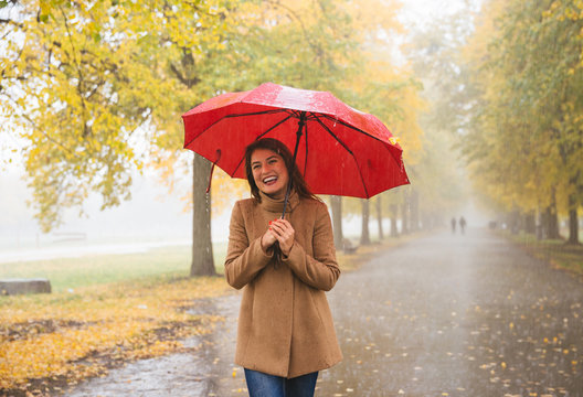 Happy woman with red umbrella walking at the rain in beautiful autumn park