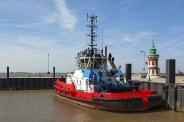 Fototapeta premium Red tugboat moored next to the historic Pingelturm lighthouse at port of Bremerhaven
