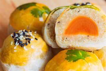 Chinese pastry or moon cake filled with mung bean paste and salted egg yolk decorated with sesame and coriander on wood cutting board in close up view, macro style. Homemade bakery concept.
