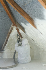 spray polyurethane foam for roof - technician spraying foam insulation using plural component gun for polyurethane foam, inside