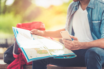 Tourist young man holding a map with the smartphone for searching direction on location map. Happy enjoying adventure travel alone by train and Tourist searching location concept