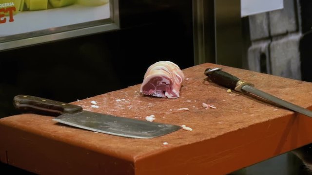 Butcher Cutting Raw Meat With Big Knife in the Market of La Boqueria. Barcelona. Spain. Slow Motion in 96 fps. Butcher cuts of beef meat at the market. A man in gloves cuts fresh, juicy beef meat on a