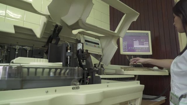 Portrait of female technician in white coat during working on computer touch screen at laboratory room, automated machine in work process, blood and urine sampleanalysis, crane shot, tracking