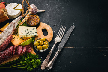 Assortment of cheeses and traditional sausages on a wooden background. Brie cheese, blue cheese, gorgonzola, fuete, salami. Free space for text. Top view.