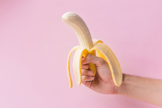 Hands peeling banana isolated on pink background.
