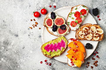 Obraz na płótnie Canvas Healthy breakfast toasts with peanut butter, banana, chocolate granola, avocado, watermelon radish, persimmon, pomegranate, chia seeds, tomato, figs, blackberry. Copy space