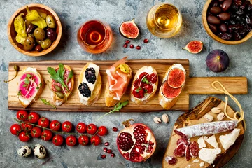 Schilderijen op glas Appetizers table with italian antipasti snacks and wine in glasses. Brushetta or authentic traditional spanish tapas set, cheese variety board over grey concrete background. Top view, flat lay © sveta_zarzamora
