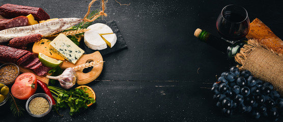 A bottle of wine, cheeses and traditional sausages on a wooden background. Brie cheese, blue cheese, gorgonzola, fuete, salami. Free space for text. Top view.