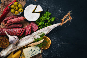 Assortment of cheeses and traditional sausages on a wooden background. Brie cheese, blue cheese, gorgonzola, fuete, salami. Free space for text. Top view.
