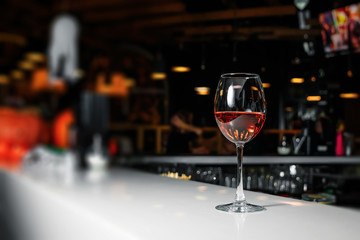 A glass of pink wine on a white bar counter against the backdrop of a restaurant