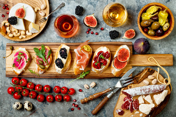 Appetizers table with italian antipasti snacks and wine in glasses. Brushetta or authentic traditional spanish tapas set, cheese variety board over grey concrete background. Top view, flat lay - obrazy, fototapety, plakaty
