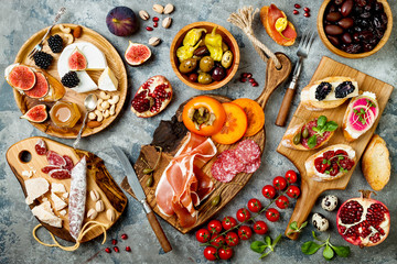 Appetizers table with italian antipasti snacks. Brushetta or authentic traditional spanish tapas set, cheese variety board over grey concrete background. Top view, flat lay - obrazy, fototapety, plakaty