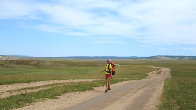Hiking woman with backpack walking along the road. Traveler girl on a hiking trail, travel and active lifestyle concept