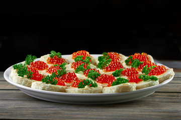 Plate full of delicious red caviar buttered canapes served on wooden table on black background copyspace eating food delicacy gourmet meny cooking appetizer concept.