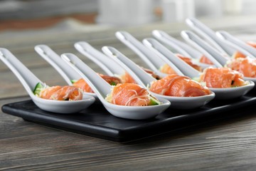Smoked salmon rolls with cheese filling served in big portion spoons on black plate on wooden table copyspace layout background delicious tasty appetizers restaurant concept.