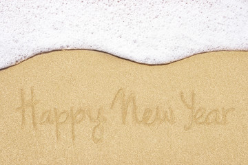 Happy new year written in sand on beach.