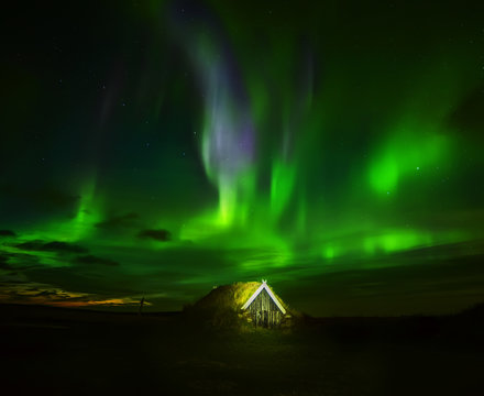 Night photo. Northern lights above the house in old traditions with grass on the roof. Iceland.
