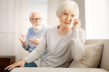 So sad. Enigmatical mature female person sitting on the foreground and using serviette while looking forward