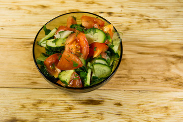 Fresh salad with tomato, cucumber, onion, parsley and dill in glass bowl on wooden table