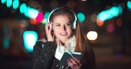 Woman with headphones using tablet and listening music in city at night