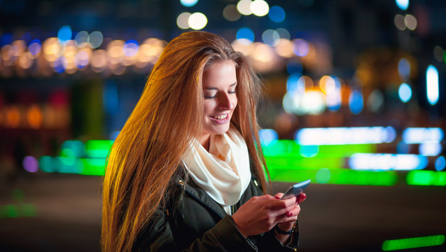 Woman using mobile phone at night in the city among neon lights
