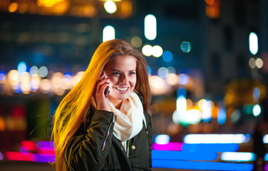 Woman using mobile phone at night in the city among neon lights