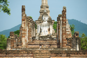 Fototapeta premium Sitting Buddha statue at the ruins of the main chapel of the Wat Mahathat temple in Sukhotai Historical Park, Thailand.