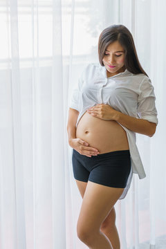 Beautiful pregnant woman standing and hand touch belly at living room. concept of pregnancy, family and lover relation.