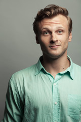 Male beauty, boy next door concept. Portrait of smiling 30-year-old man standing over gray background. Close up. Classic style. Wavy glossy blond hair. Text space. Studio shot